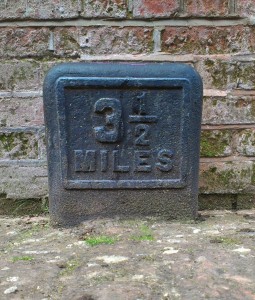 Cast-iron milepost set in canal towpath against a brick wall